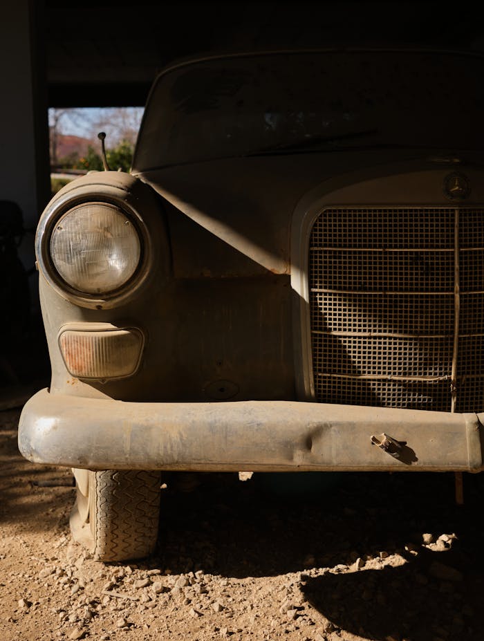 Front view of an old dusty car in a dimly lit garage, showcasing vintage design.
