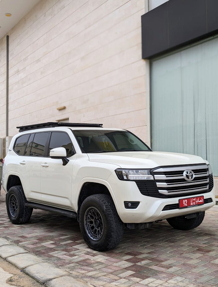A white SUV parked on a sidewalk in Salalah, Oman with Arabic license plate.